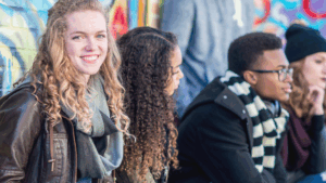 Group of seated teenagers, one smiling at the camera and three looking away